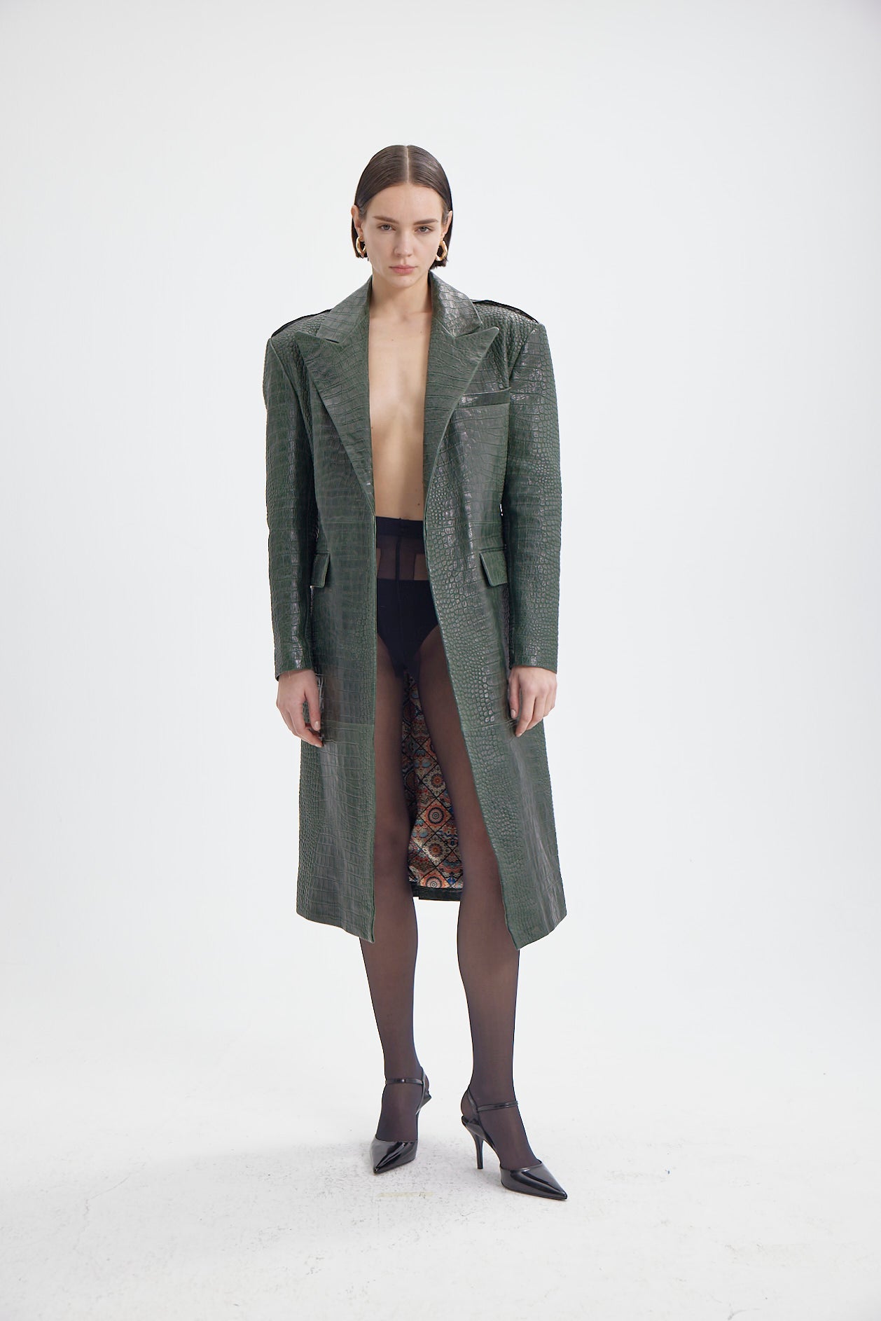 Woman showcasing a sophisticated green croco-embossed leather coat with a waist belt and detailed design.