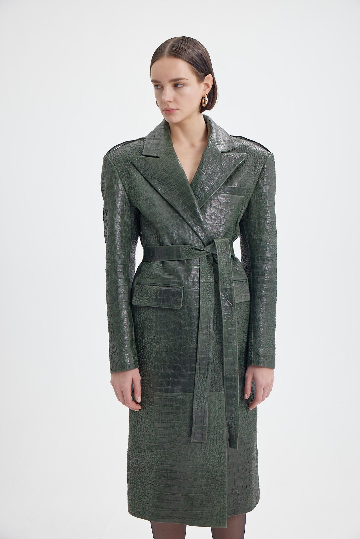 Woman showcasing a sophisticated green croco-embossed leather coat with a waist belt and detailed design.