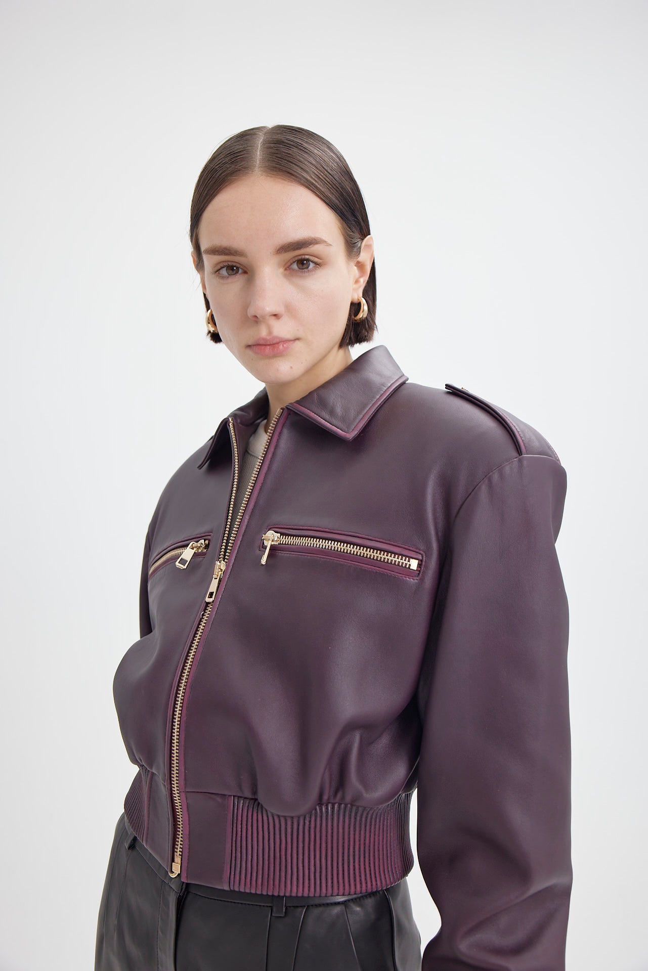 Close-up of model wearing DREJANI Burgundy Silky Short Bomber, highlighting the gold-tone hardware and silky leather texture.